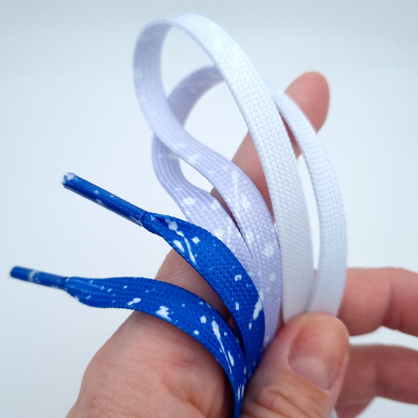 Hand hält Schnürsenkel mit Farbverlauf in Blau Weiß.